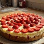 Realistic photo of a homemade strawberry cheesecake on a kitchen counter, featuring fresh strawberries on top and a slightly uneven crust, captured in natural lighting with a cozy, lived-in kitchen background. Perfect for showcasing a casual, homemade dessert.